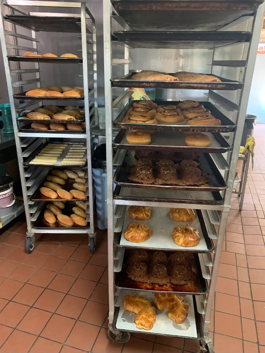 Bakery racks of trays fresh from the ovens — rolls, cinnamon rolls, donuts, pastries and cakes