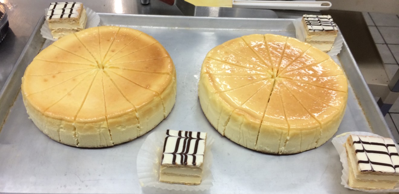 Two whole cheesecakes, sliced and glazed, with individual dessert squares on a sheet tray